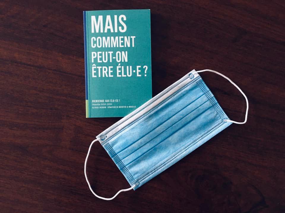 un livre dont le titre est "mais comment peut-on être élu-e?" et un masque chirurgical posés sur une table